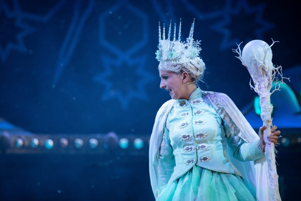 The snow queen is pictured screaming at someone below. She has an ice crown and is holding a stalk with a ball on top.