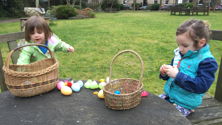 Two girls sit opening plastic Easter eggs filled with small toys. They are in a private Edinburgh garden.