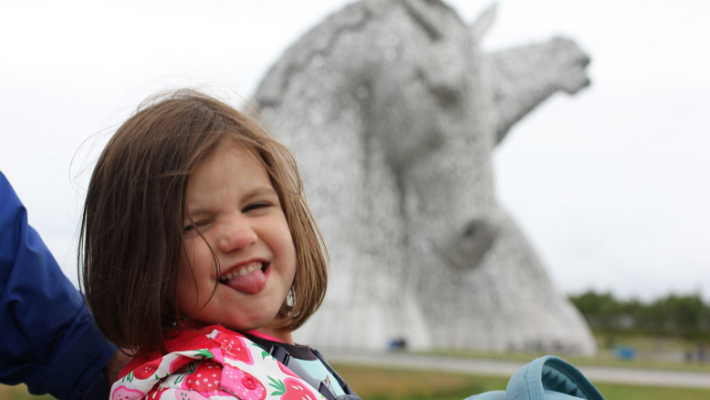 A small girl sticks her tongue out in front of the Kelpies Statues in Helix Park.