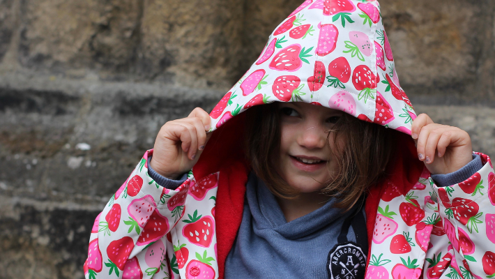 A girl wearing a Hatley rain coat with the hood up.