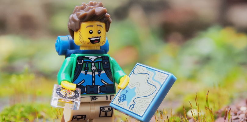 A lego figure holding a map. The background is blurred and looks like a forrest.