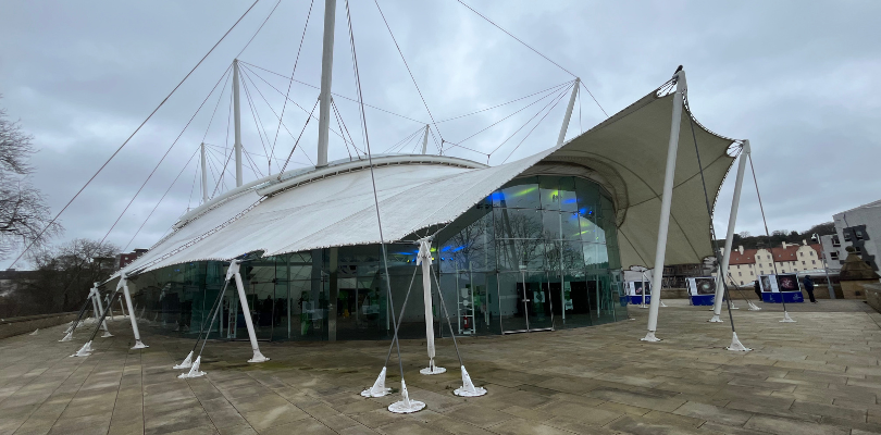 An image of Dynamic Earth Edinburgh from the outside. The sky is grey and it was been raining.